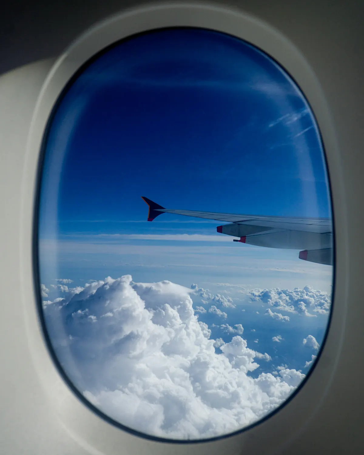 Aircraft wing over the clouds seen through an oval cabin window