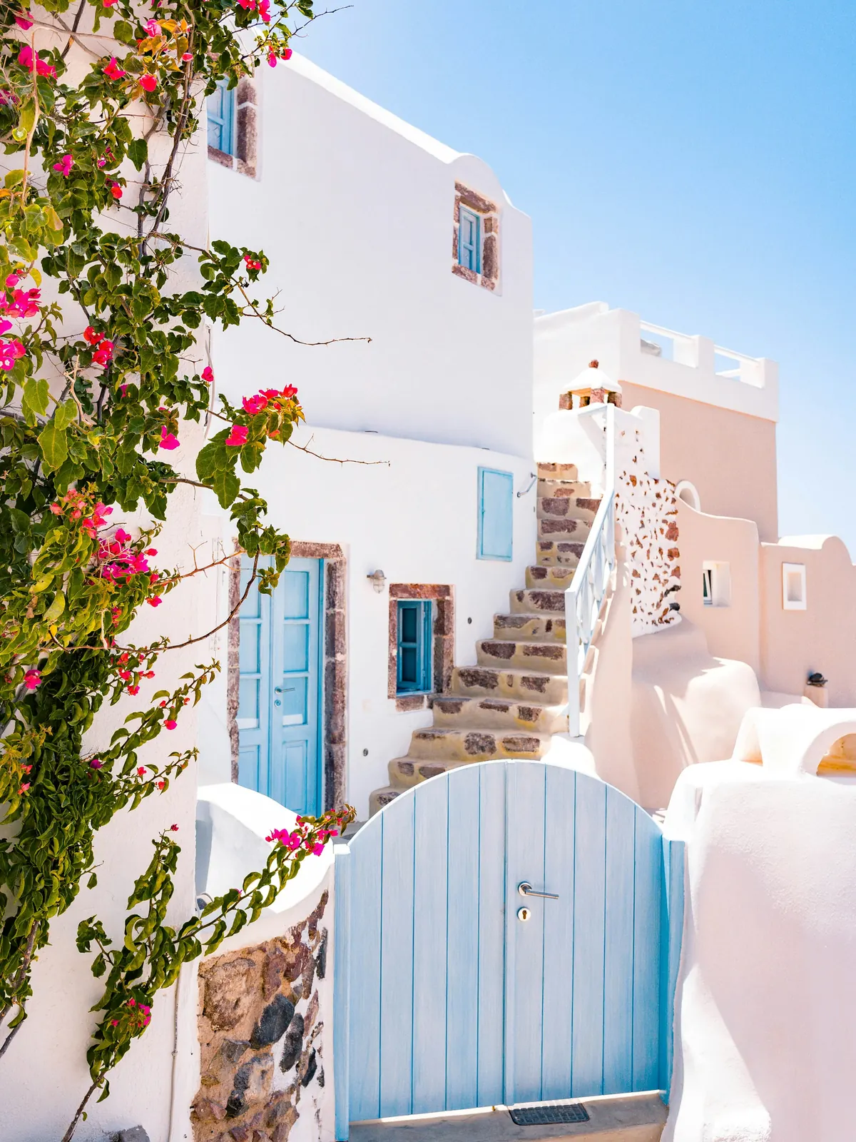 Blue wooden gate framed by bougainvillea on a whitewashed lane